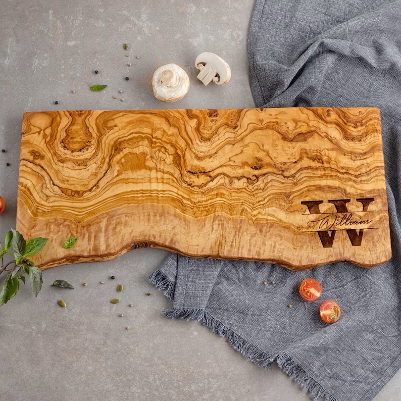 Live edge cheese board made out of olive wood with a monogram engraved in the lower right corner.