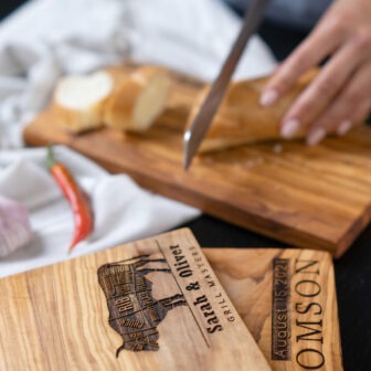 A person is slicing a piece of bread on a Personalized Wooden Cutting Board.