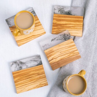 Top-down view of two cups of coffee on wooden and marble coasters arranged on a white textured surface.