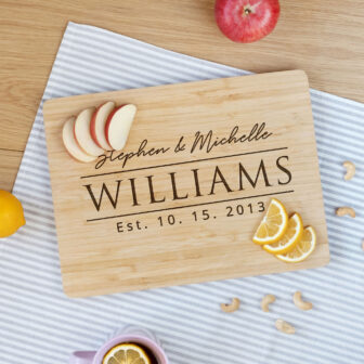 Personalized cutting board with the names "stephen & michelle williams" and the date "10.15.2013," surrounded by sliced fruit and nuts on a kitchen countertop.