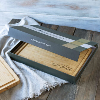 A bamboo cutting board with its packaging placed on a wooden surface with a cloth underneath.