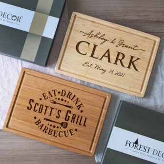 Personalized wooden cutting boards with engraved names and motifs, shown alongside their packaging.