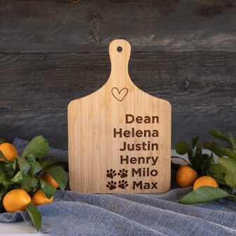 Personalized cutting board with names and paw prints alongside fresh citrus fruit on a wooden table.
