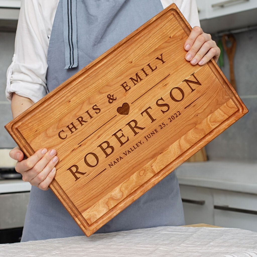 A woman holding up a wooden cutting board with the name chris and emily robertson.