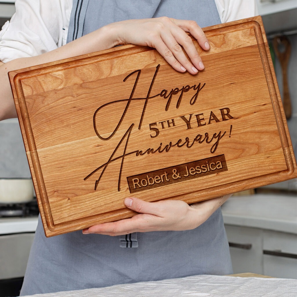 A woman holding a cutting board that says happy 5th anniversary.