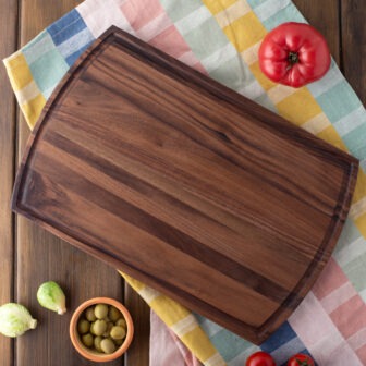 A Wood Cutting Board with Juice Groove & Arched (Walnut - 16x10) with olives and tomatoes on it.