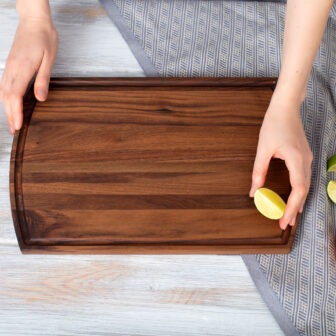 A person holding a Wood Cutting Board with Juice Groove & Arched (Walnut - 16x10) with lemons on it.