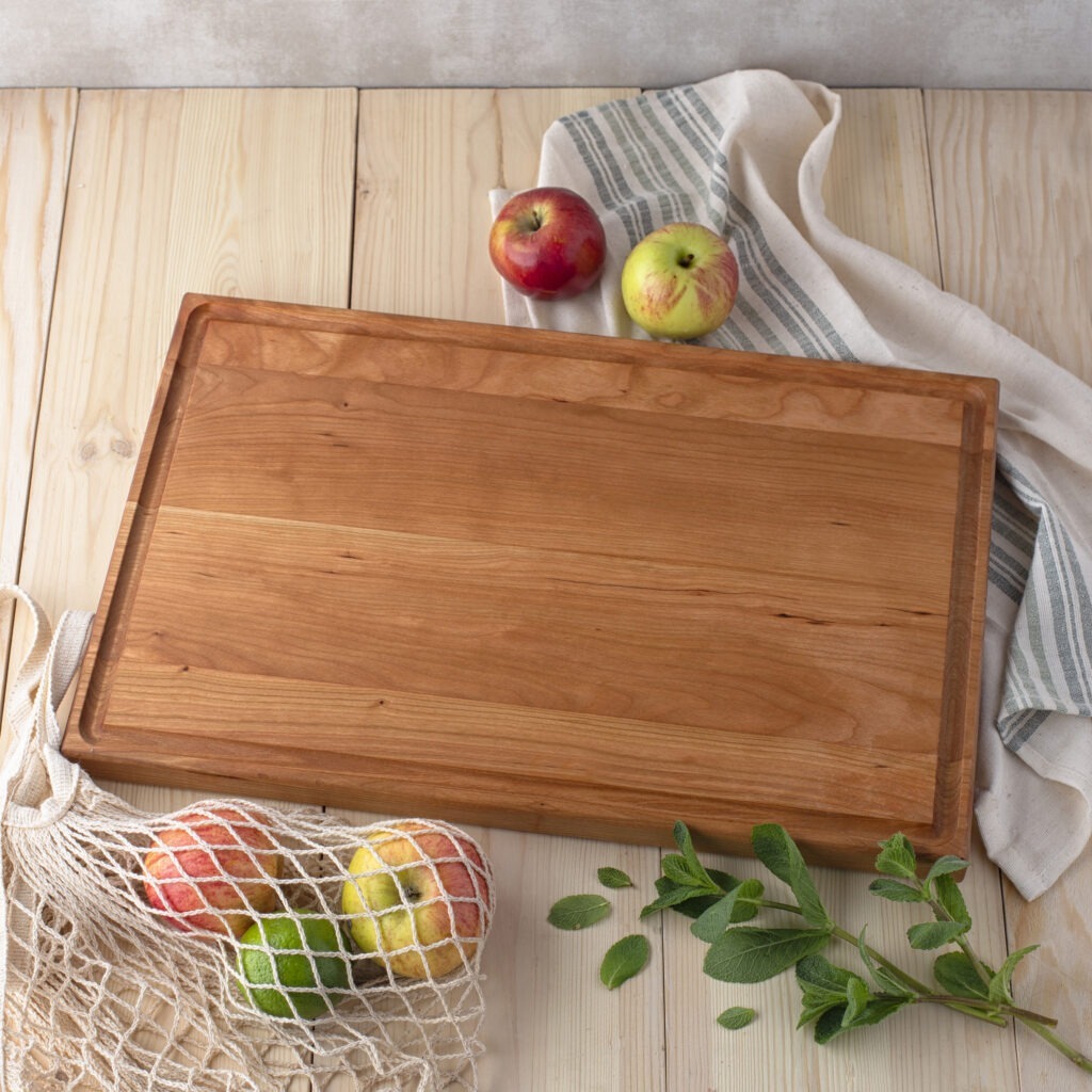A juice groove cutting board on a wooden table with apples and a net.