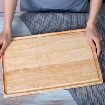 A woman holding a juice groove cutting board on a table.