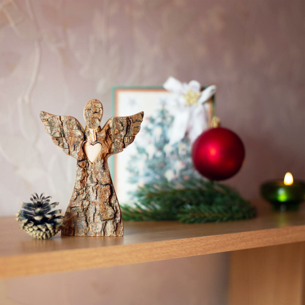 A wooden angel sits on a shelf next to a christmas tree.