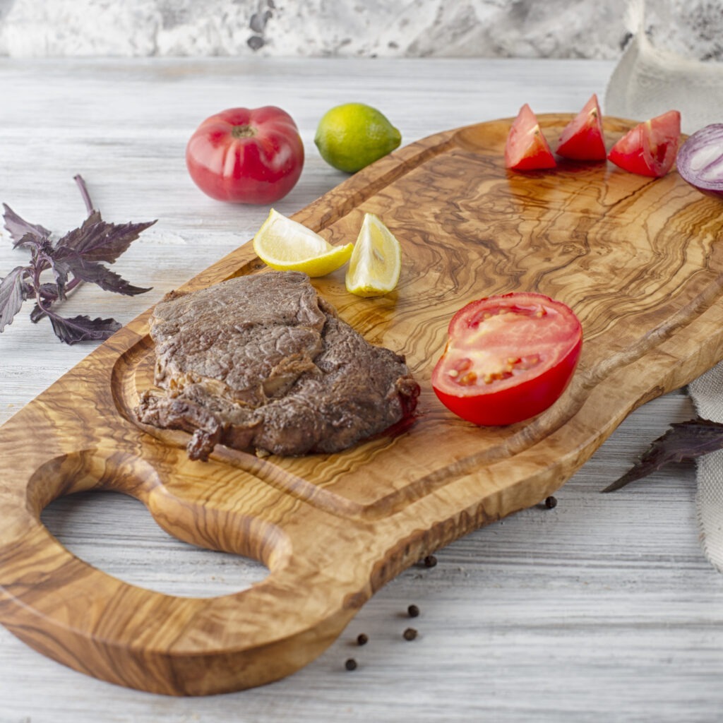 A wood serving board with handle with a steak on it.