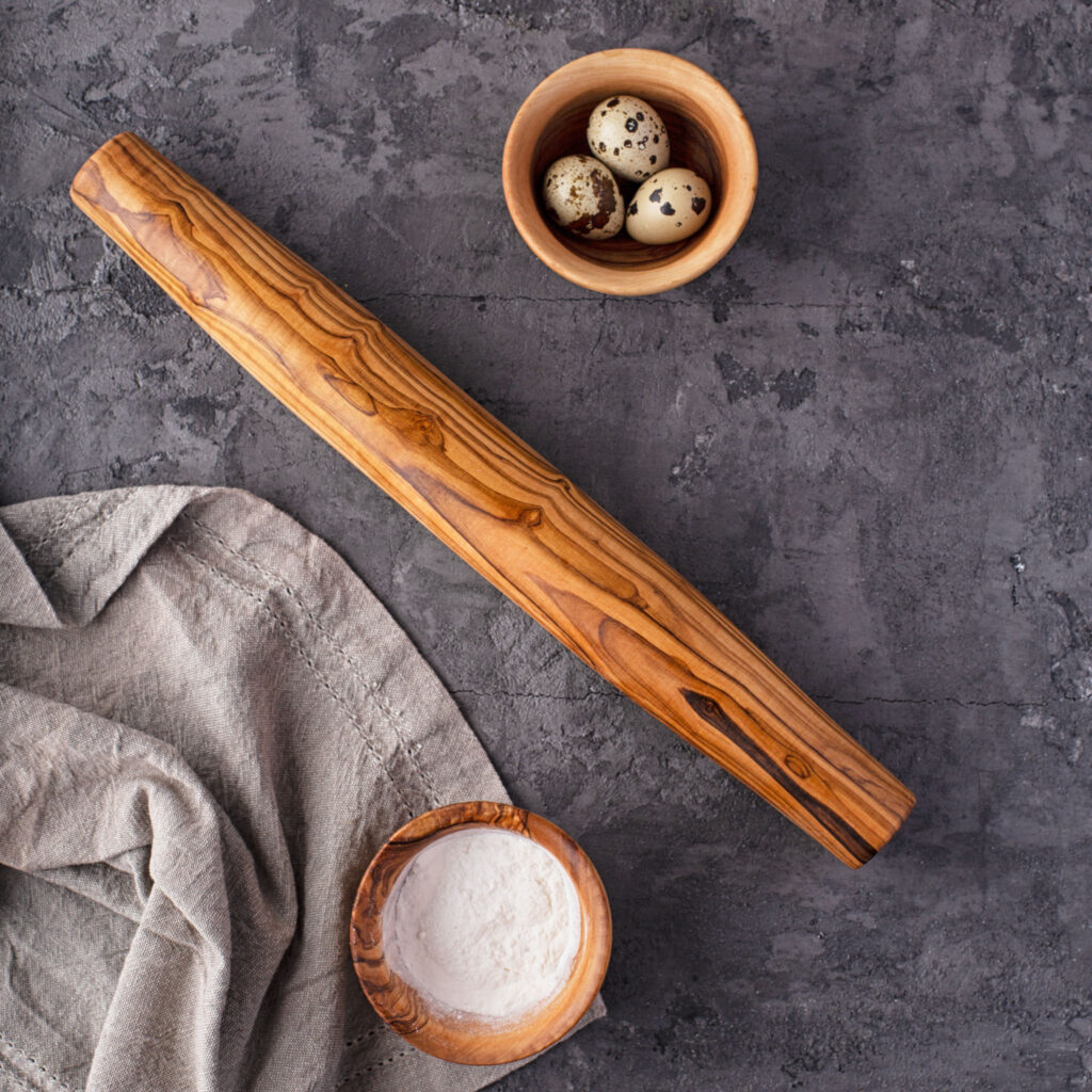 A wooden rolling pin and a bowl of eggs on a gray background.