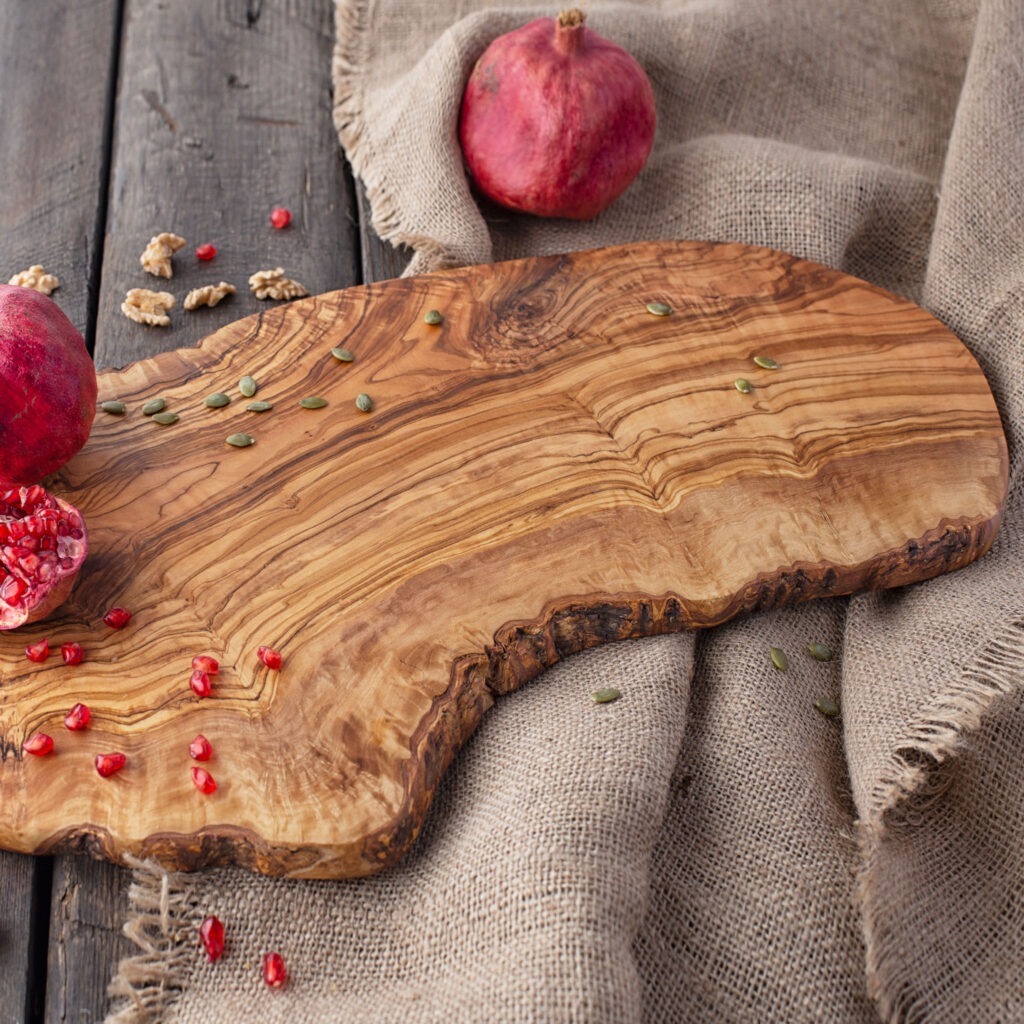 A olive wood live edge board with pomegranates and pomegranate seeds.