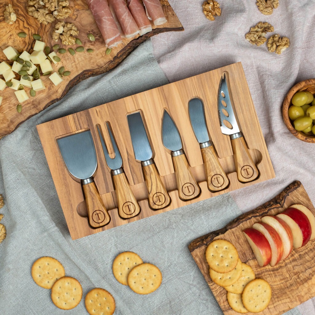 A cheese board with a set of knives and assorted snacks displayed around it.