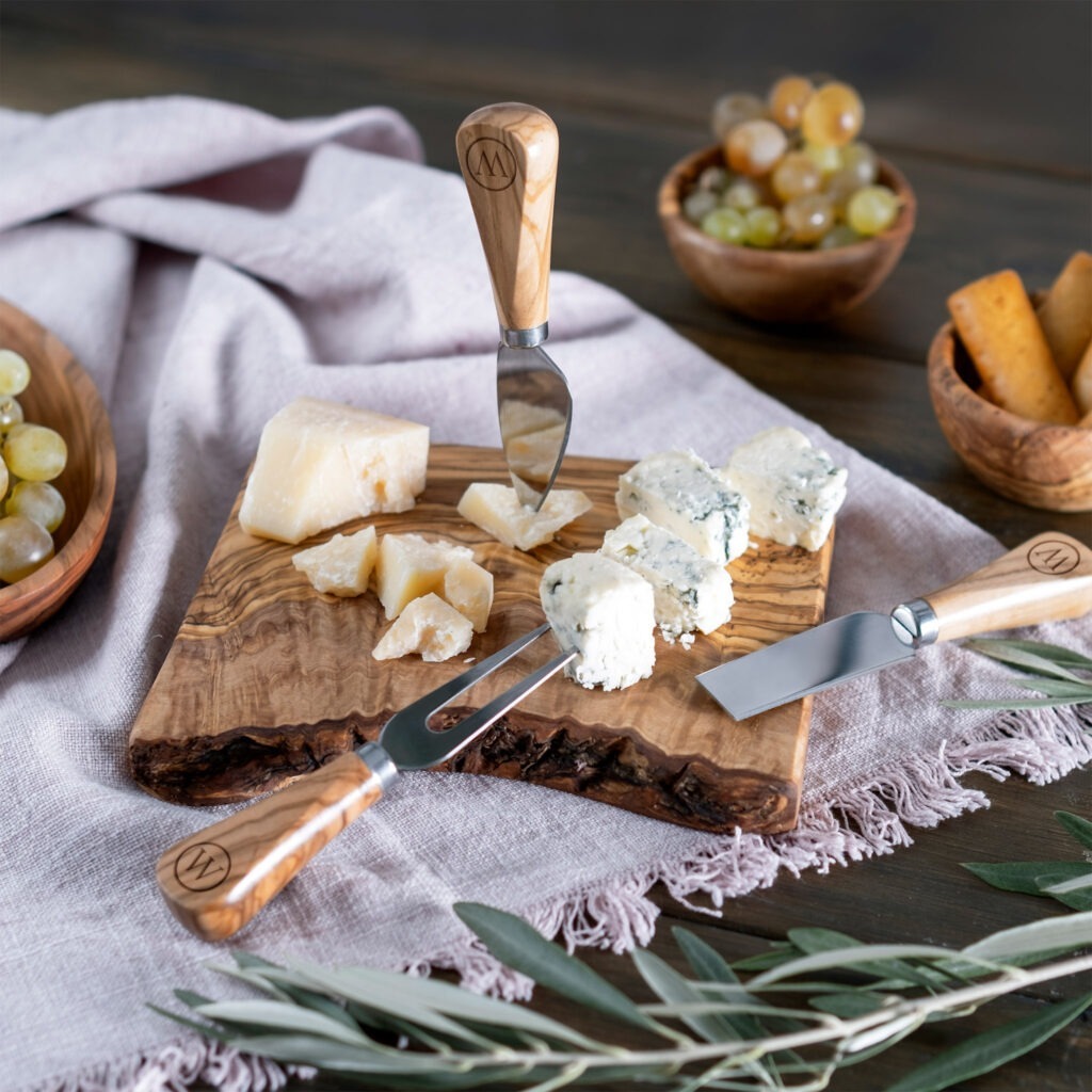 A wooden board with cheese, grapes and olives.
