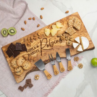 A personalized wooden cheese board with assorted snacks and cheese knives on a marble countertop.
