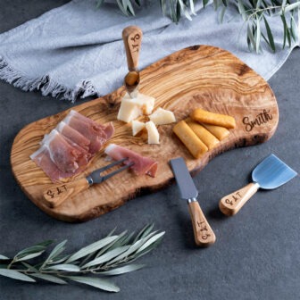 A wooden cheese board with cheese and olives on it.