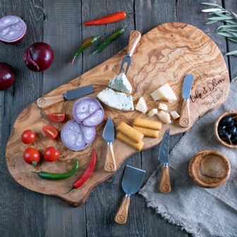 A wooden cutting board with cheese, vegetables, and utensils.
