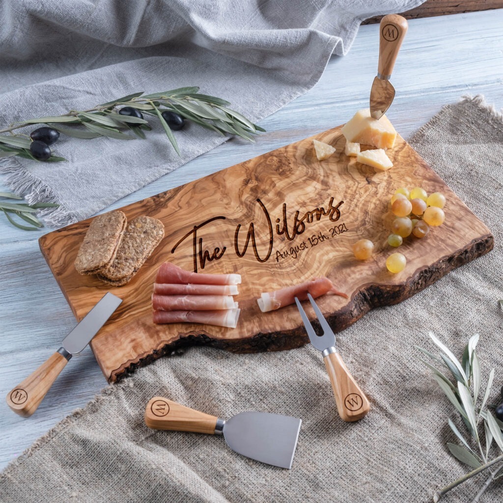 A wooden cutting board with cheese, olives, and utensils.