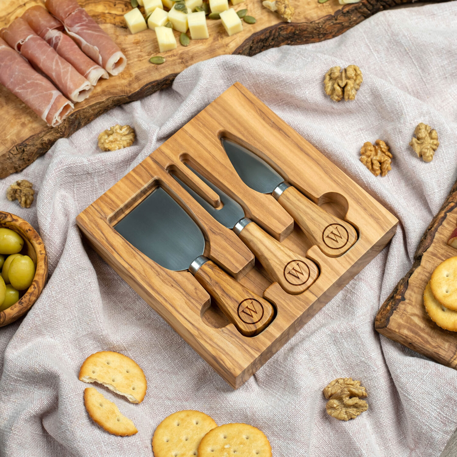 A cheese board with knives on a table surrounded by various appetizers.
