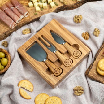 A cheese board with knives on a table surrounded by various appetizers.