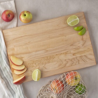 A Wood Cutting Board (Maple) with apples and limes on it.