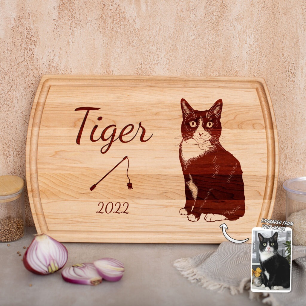 A wooden cutting board with a personalized engraving of a cat named tiger, dated 2022, placed on a kitchen counter.