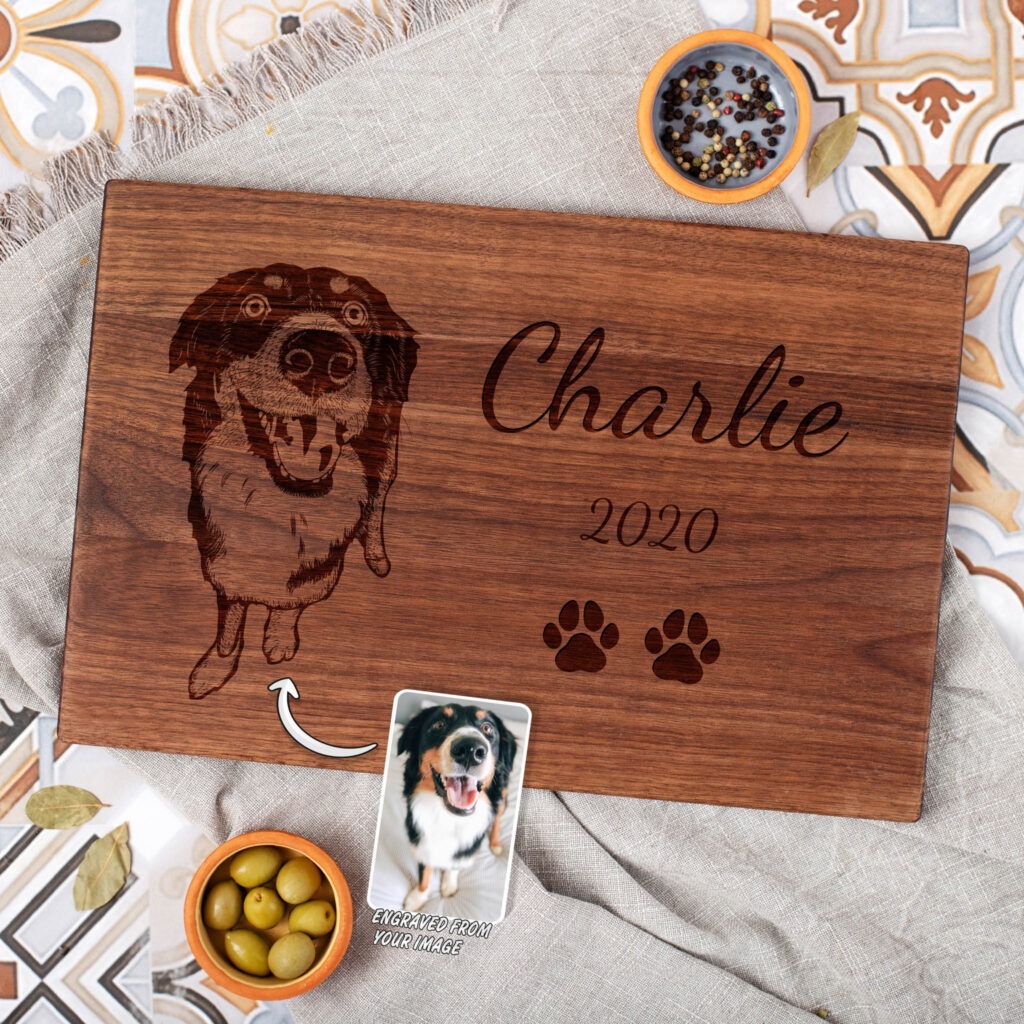 Custom engraved wooden board featuring the name "charlie," a date "2020," a dog's image, and paw prints alongside a photograph of the dog.