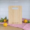 A wooden cutting board with a placeholder text for a logo, positioned on a pink cloth with lemons nearby.