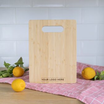 A wooden cutting board with a placeholder text for a logo, positioned on a pink cloth with lemons nearby.