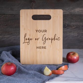 A wooden cutting board with placeholder text for customization, accompanied by apples on a kitchen countertop.