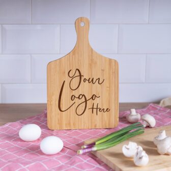 Wooden cutting board with customizable logo, accompanied by eggs, mushrooms, and green onions on a kitchen countertop.