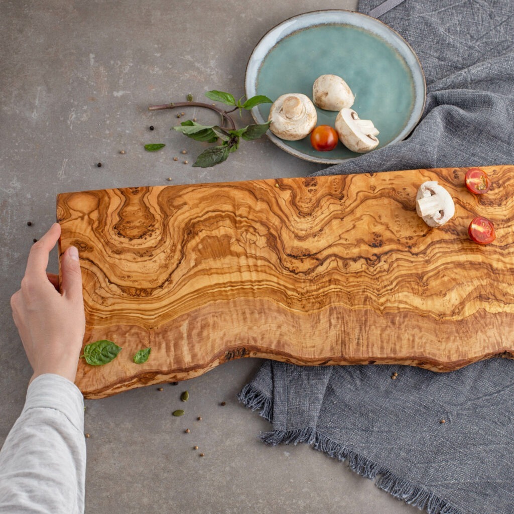A person is holding an olive wood cutting board.