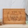 A wooden cutting board with the words'13th anniversary lucas and olivia'.