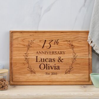 A wooden cutting board with the words'13th anniversary lucas and olivia'.