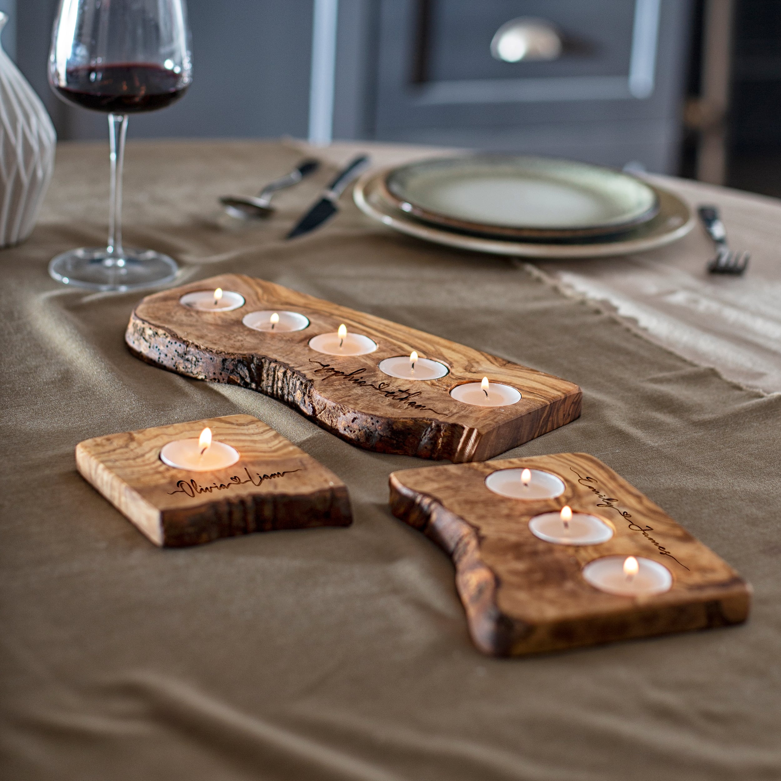 Rustic wooden candle holders with lit tea candles on a table, set beside a wine glass and dinnerware.