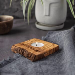 A wooden candle holder with a lit tealight on a gray textile surface, accompanied by a ceramic vase and bowl.