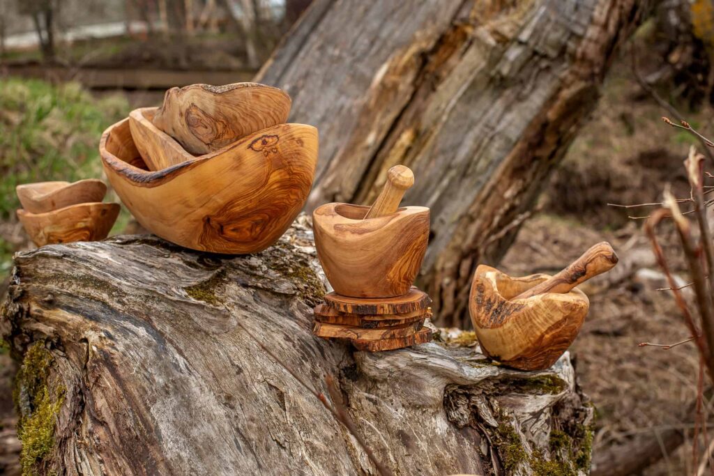 Handcrafted wooden bowls and a pestle displayed on a fallen tree trunk in a rustic outdoor setting.