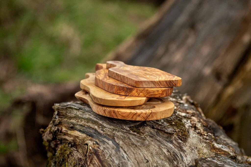 A stack of handcrafted wooden coasters with a unique grain pattern, resting on a textured tree trunk in a natural setting.