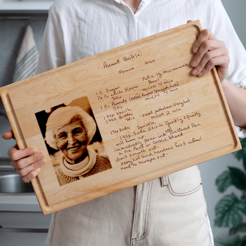 A woman is holding an engraved recipe cutting board with a photo of her grandmother.