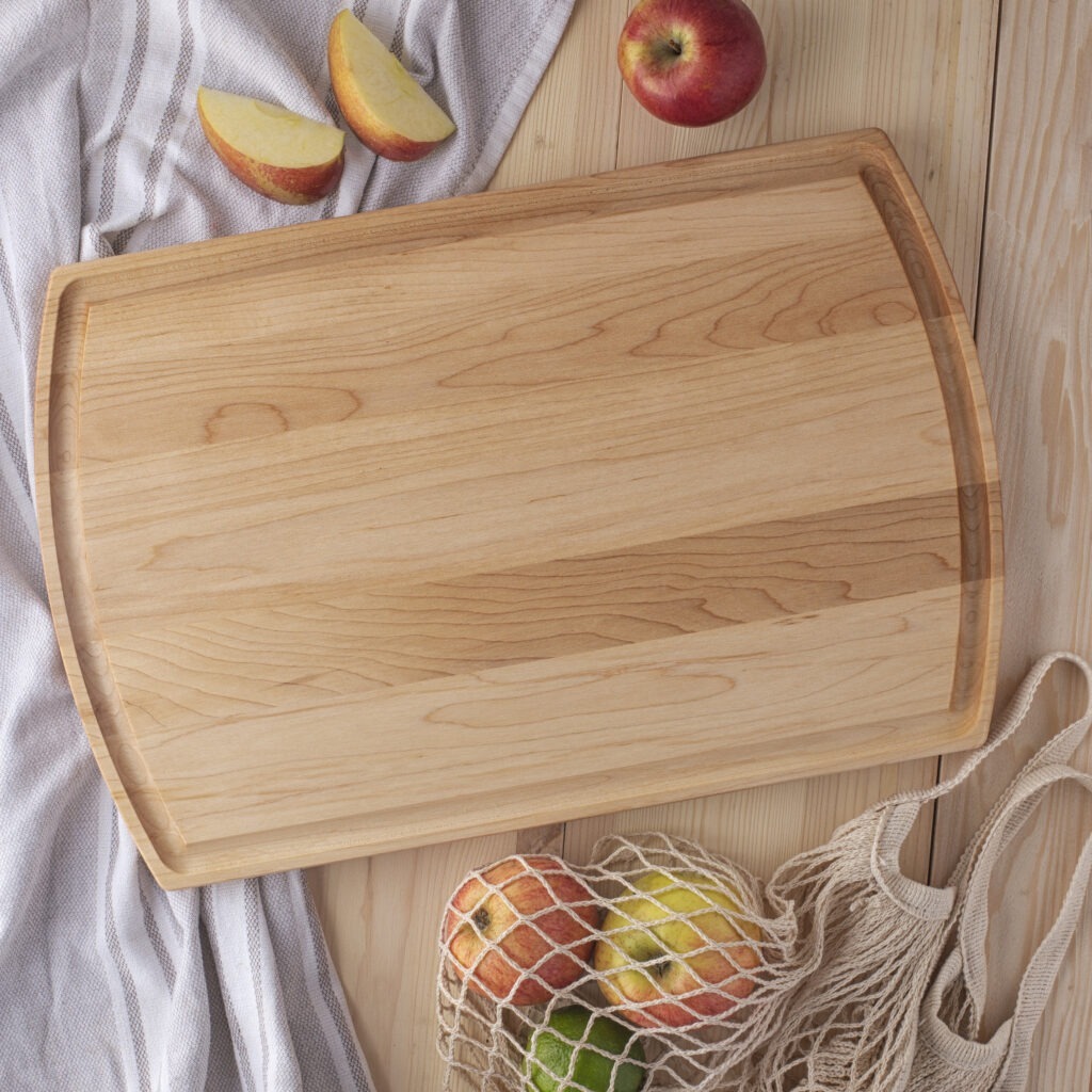 A rustic wooden cheese boards with apples and a bag of apples.