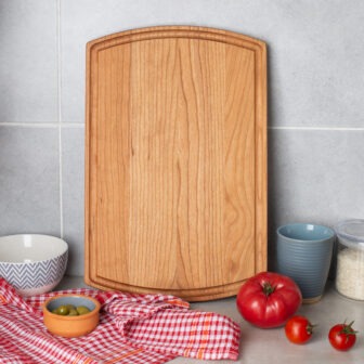 A Large Wood Cutting Board with Juice Groove & Arched (Cherry- 16x10) on a kitchen counter.
