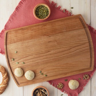 A Cutting Board with Juice Groove & Arched with nuts and seeds on it.