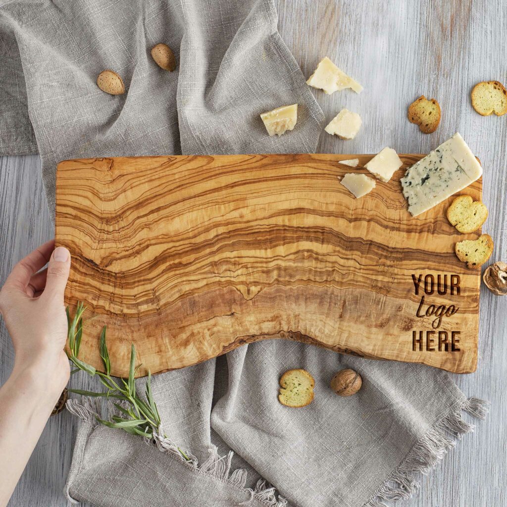 A person holding a custom charcuterie logo cutting board made out of olive wood.