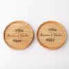 Two round wooden coasters engraved with the names Martin & Emilia, the years 1982-2022, and decorative leaf flourishes.