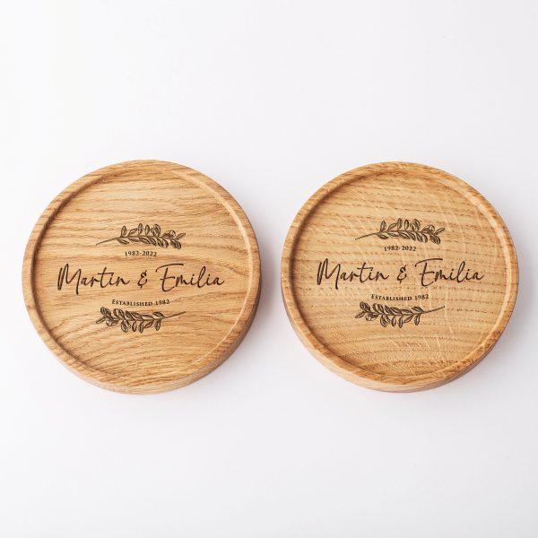 Two round wooden coasters engraved with the names Martin & Emilia, the years 1982-2022, and decorative leaf flourishes.