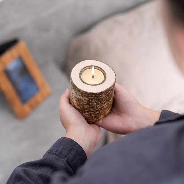 Hands holding a birch log candle holder with a lit tea light